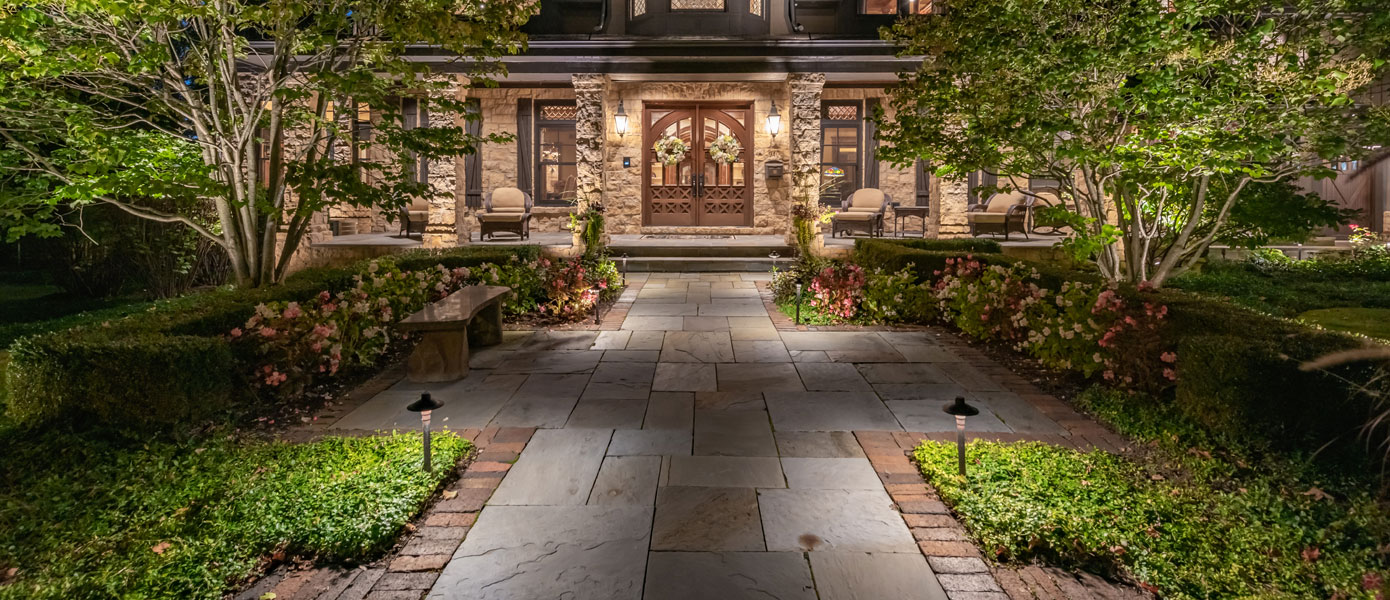 A stone walkway with trees and a doorDescription automatically generated