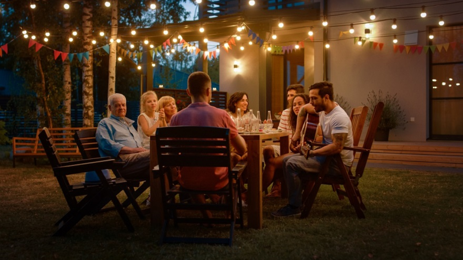 family having a dinner together outside in backyard with string lighting above them