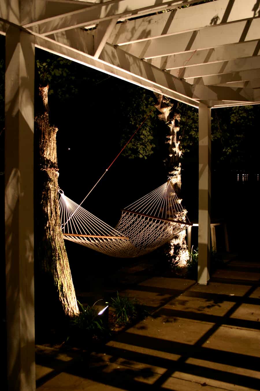 a backyard hammock next to trees that have halogen lights illuminating them