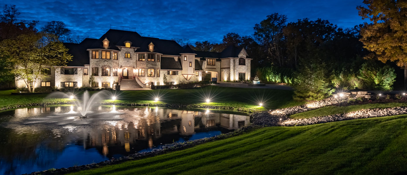 home with landscape lighting around pond