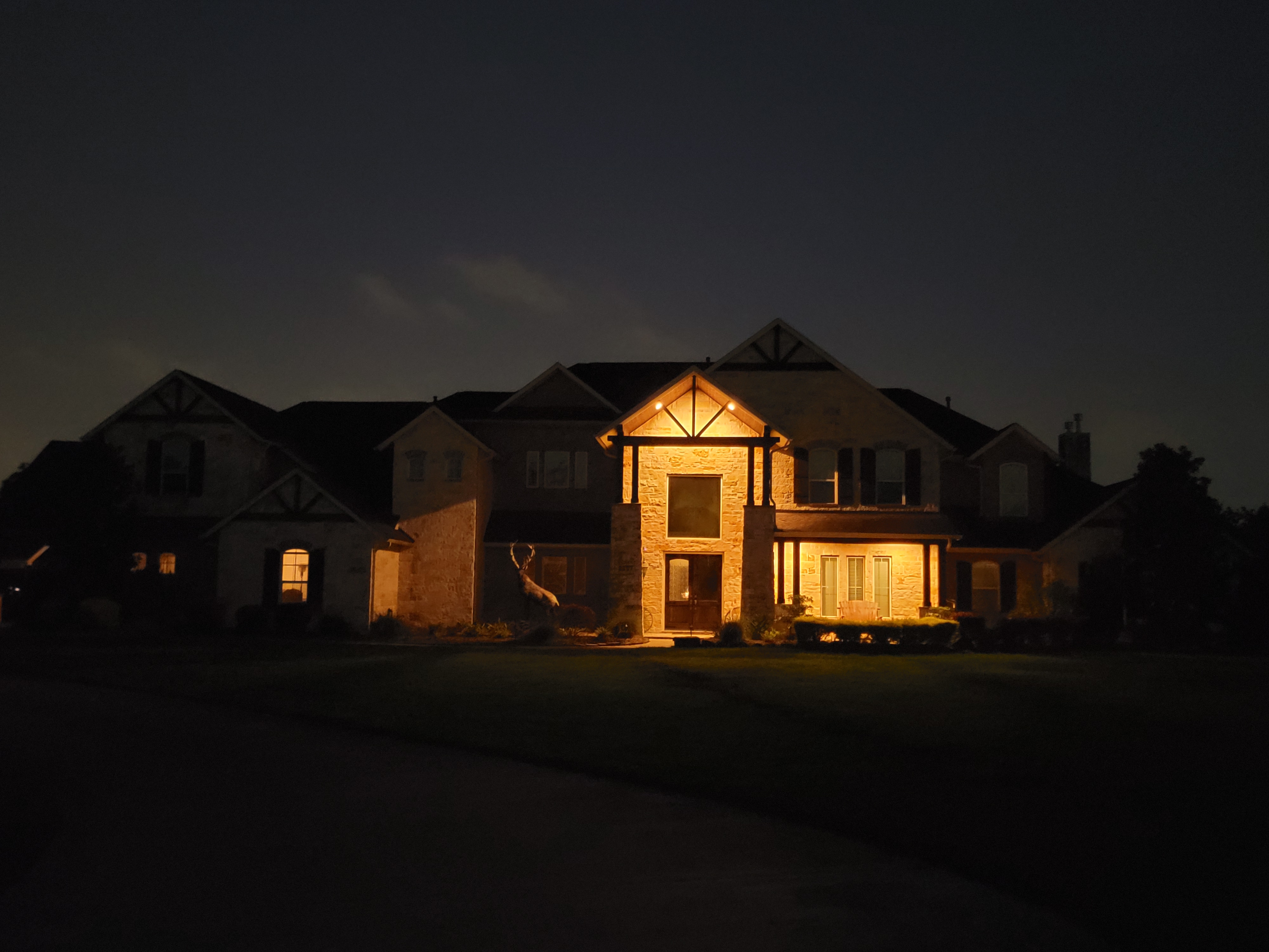A side-by-side comparison of a Houston residential property before and after a professional landscape lighting installation, featuring warm LED architectural uplighting and pathway safety lights.