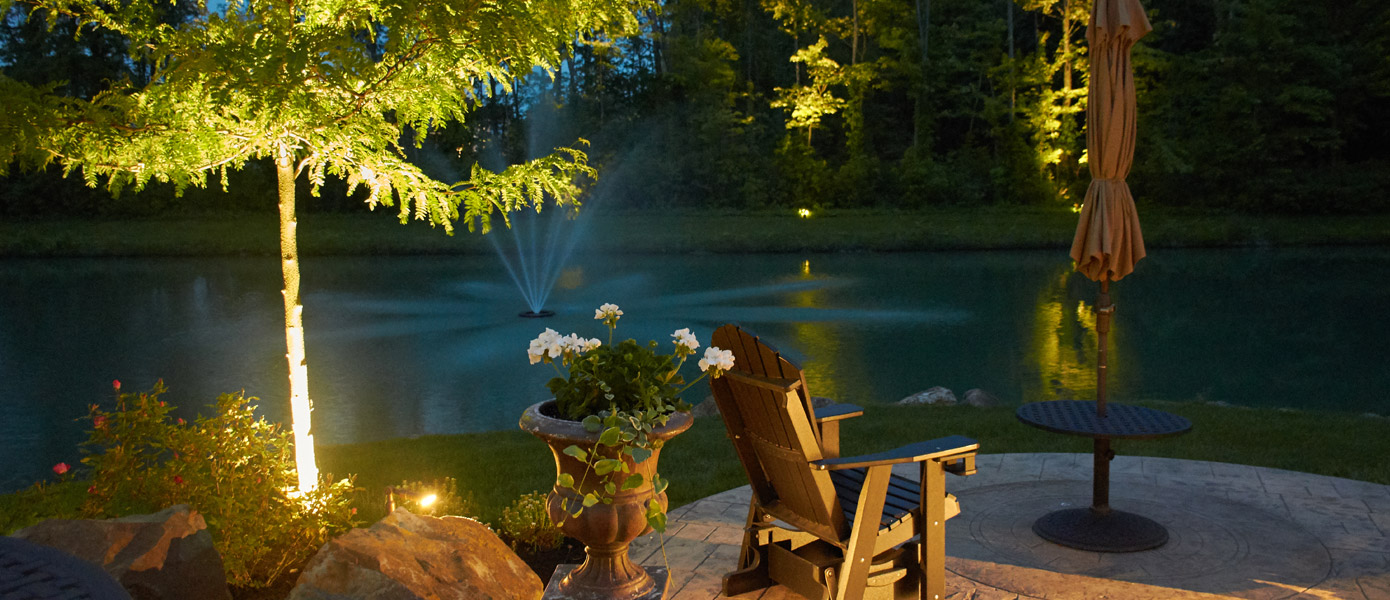outdoor seating area in front of pond with lit trees