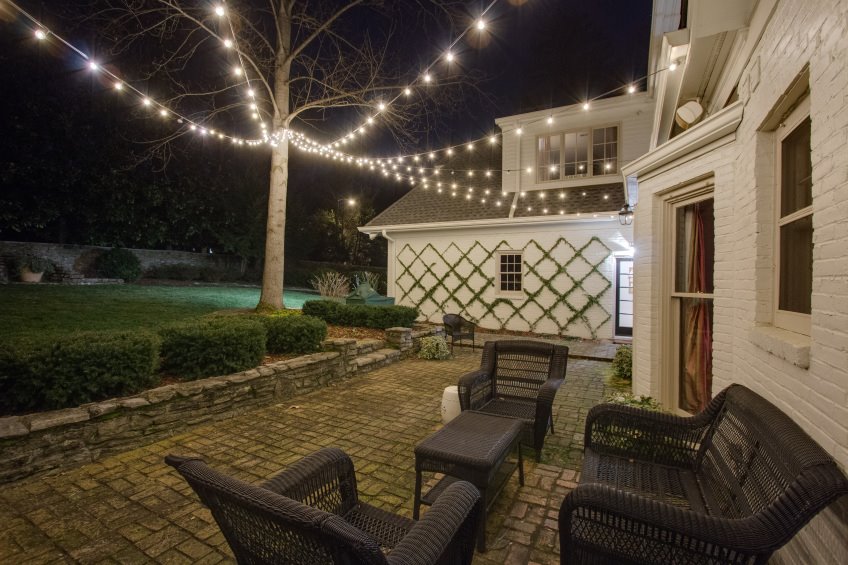 patio seating area lit by string lighting attached to tree and house