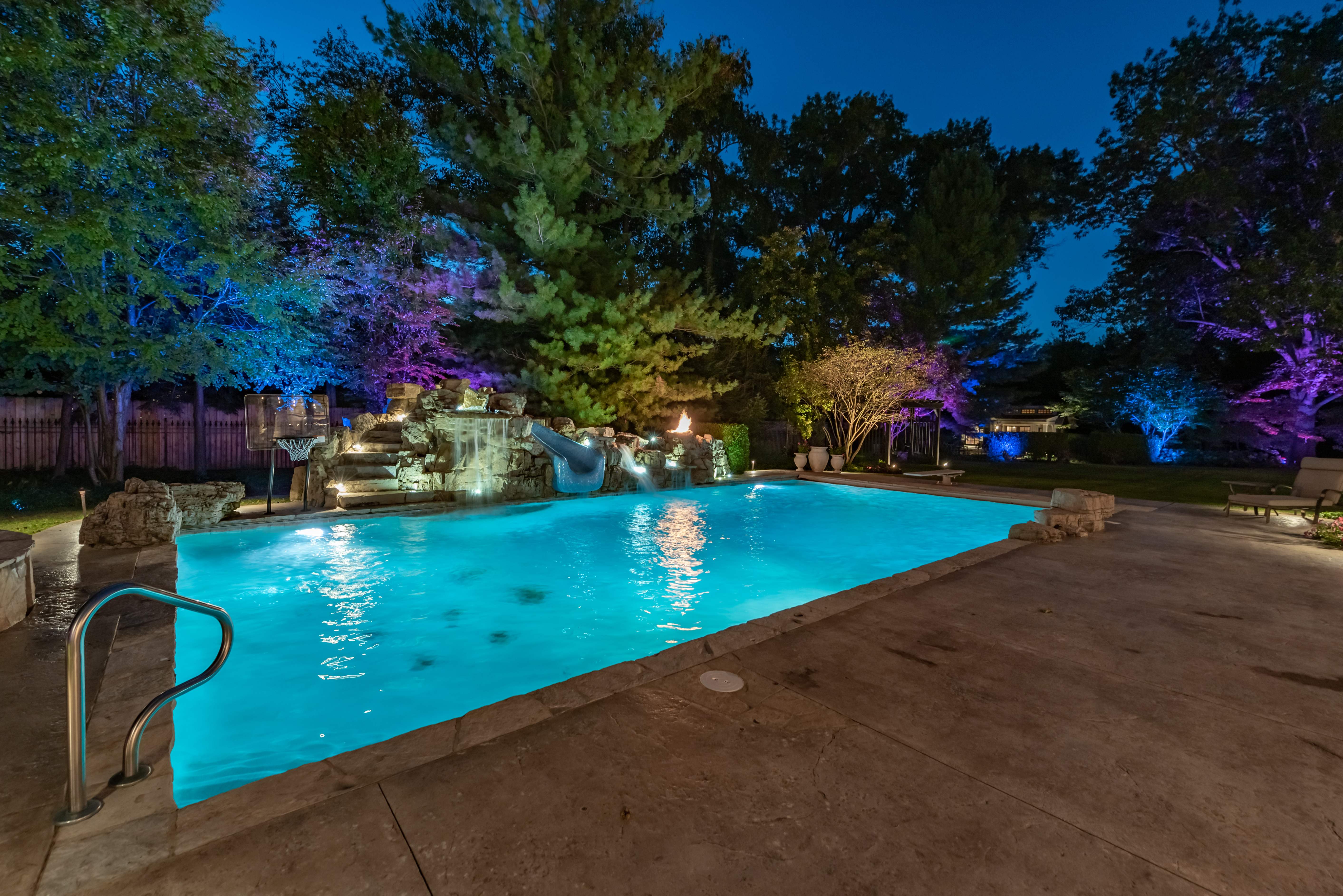 A pool with a fountain and trees at nightDescription automatically generated