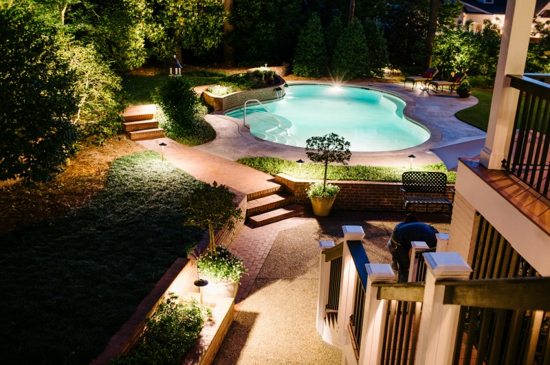 backyard and pool lit by outdoor lighting
