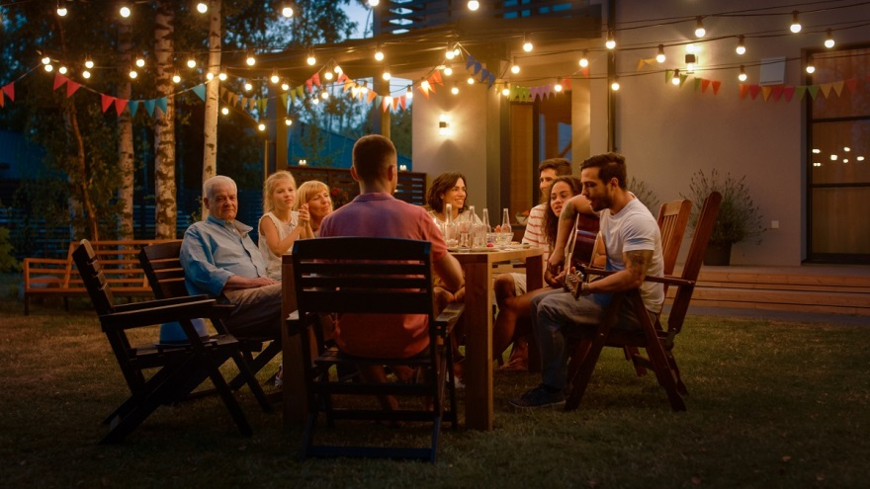 group of people around a table at outdoor patio with string lighting 