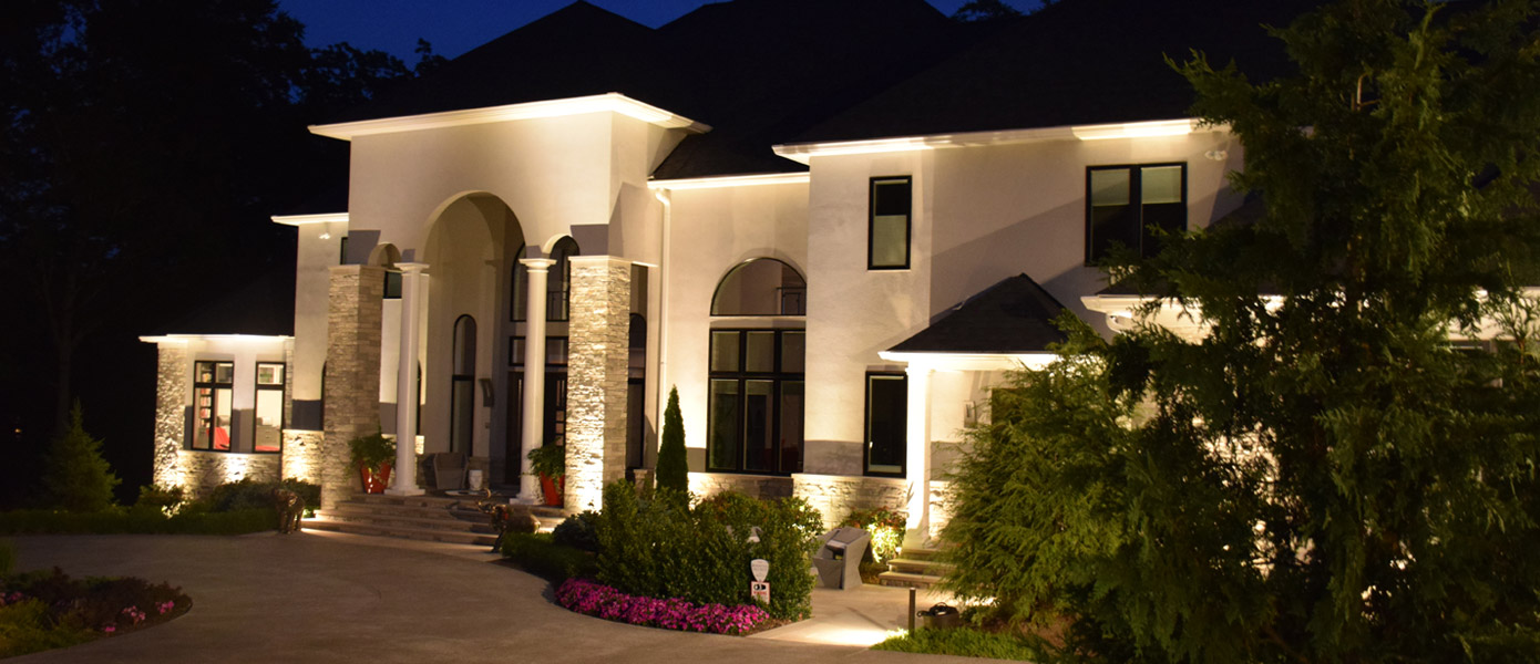 architectural lighting on the front of a white house with stone accents and trees