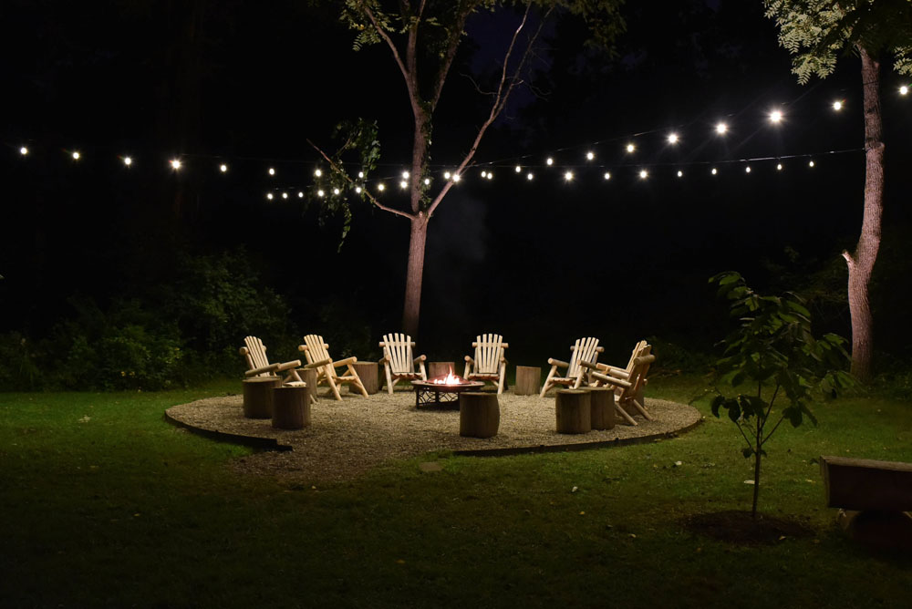 Festive string lighting in a yard with a firepit and chairs