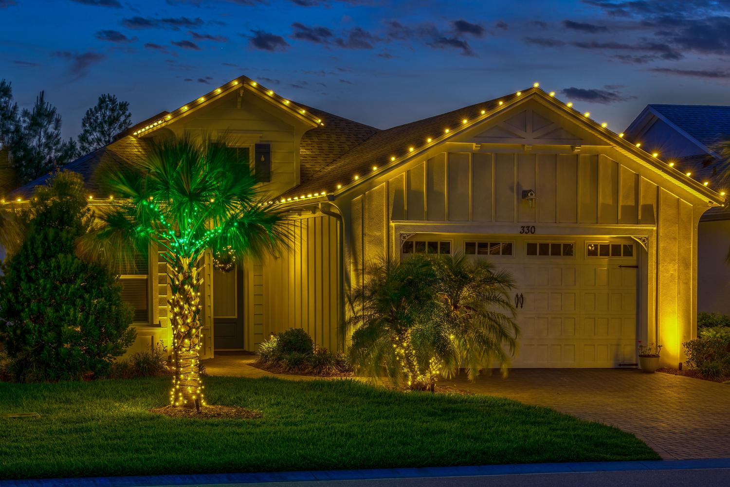 A home, garage, and palm tree decorated with yellow and green holiday lights in Irvine, California
