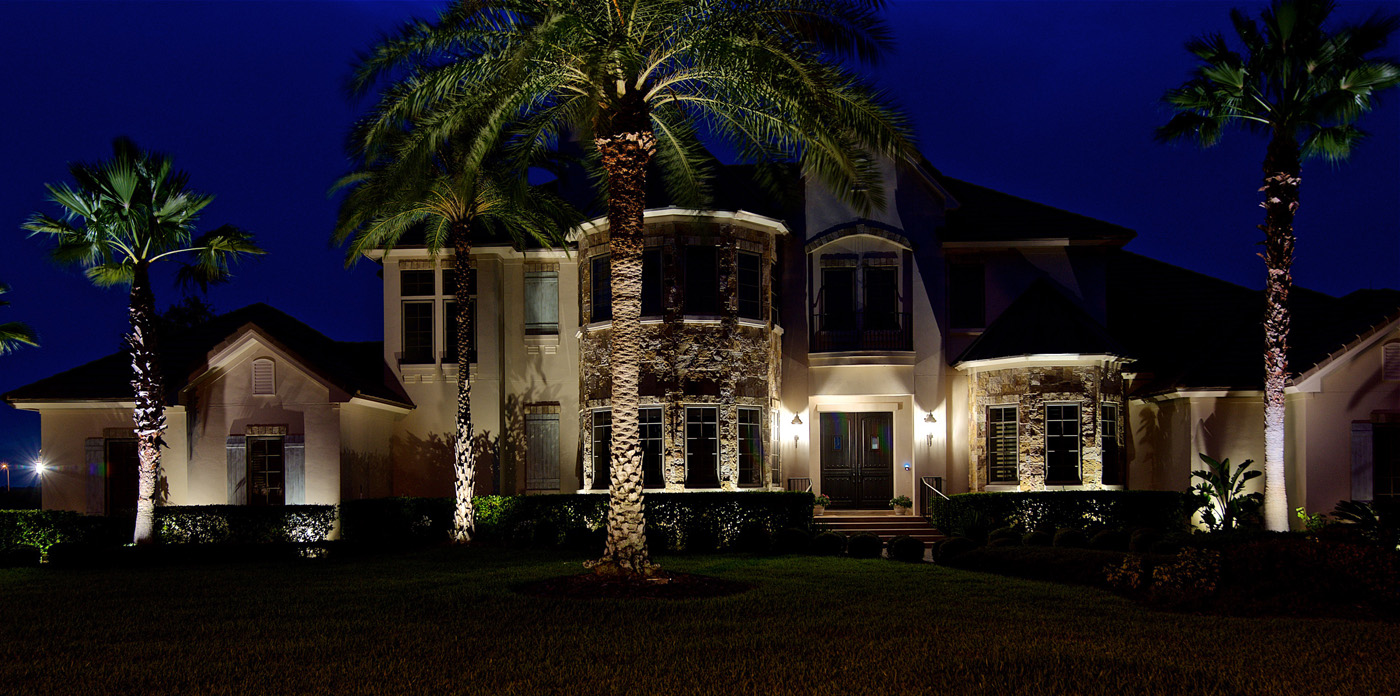 front of a house lit by architectural lighting and palm trees lit 