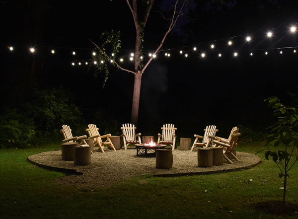 chairs arranged in a circle around a fire it with string lighting above them