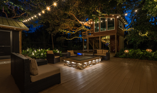 A deck with a fire pit and a tree with lightsDescription automatically generated