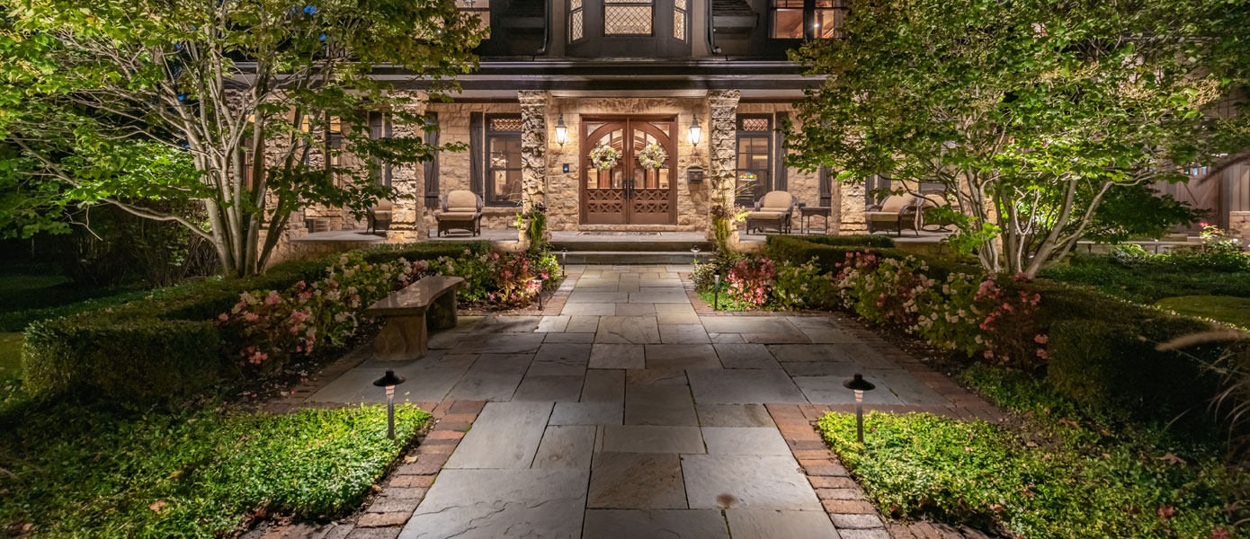 A stone walkway with trees and a doorDescription automatically generated