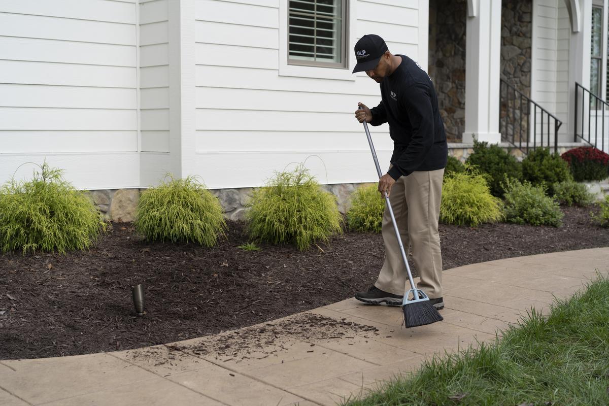 a man brushing mulch back into flower beds with a broom